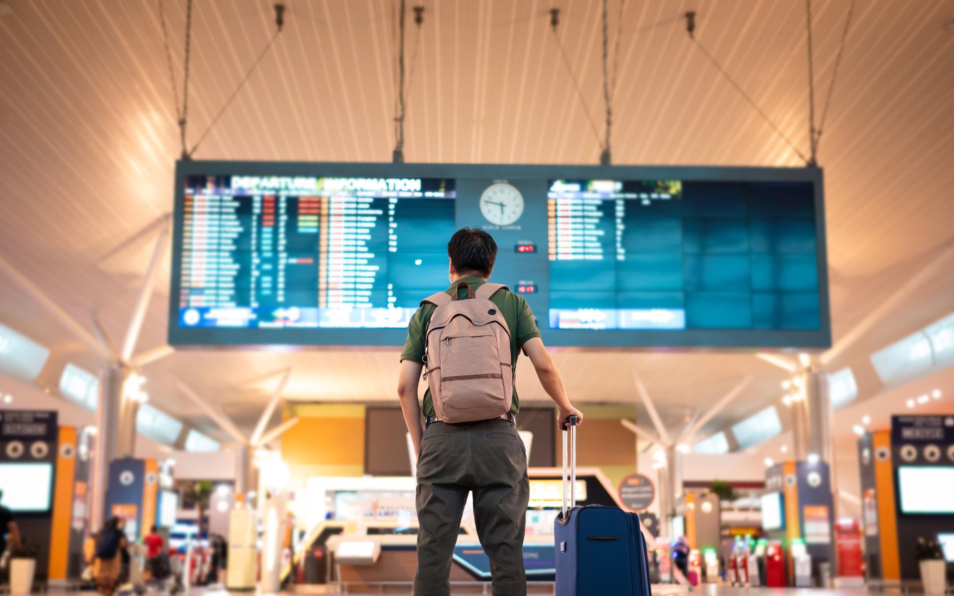 Eine Person blickt auf die Abflugtafel an einem Flughafen. 
